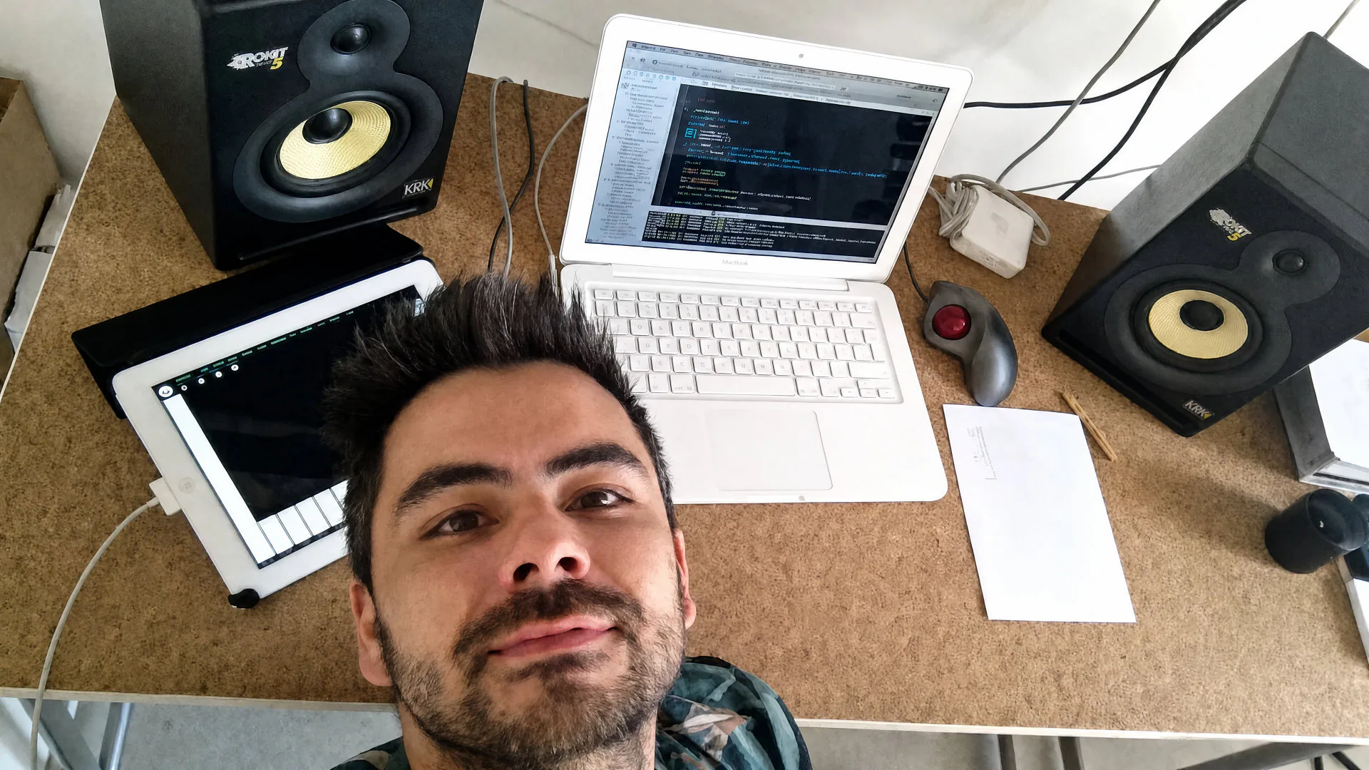 2014年、作業台に向かう Nuno — 2台の KRK Rokit 5 モニターに挟まれて Xcode を 動かす白い MacBook、ノートパソコンの下には初期のアプリを表示した iPad、 キーボードのそばにはトラックボールマウス。