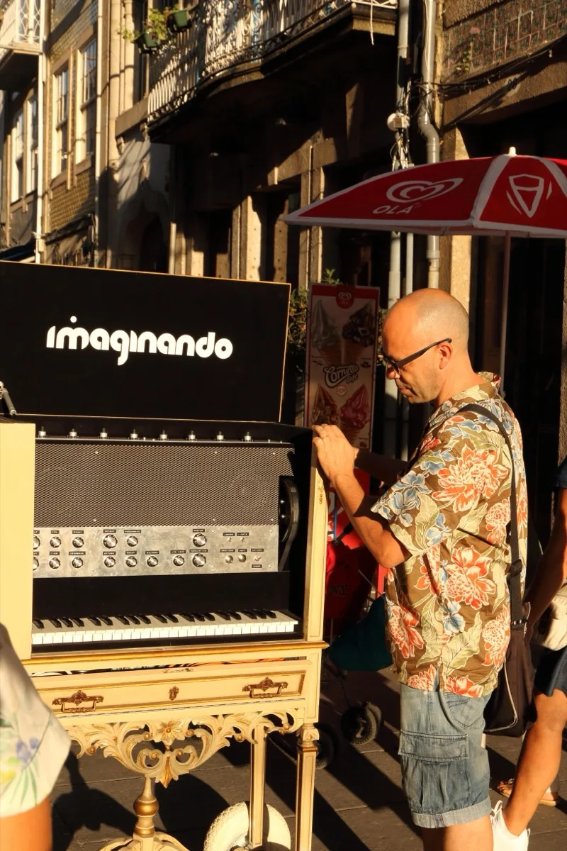 夕暮れの Braga の通りで、花柄のシャツの男性が Digital Music Box の前で 足を止め、上がった「imaginando」の蓋に片手を添えている。